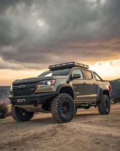 the truck is driving down the dirt road with dark clouds in the sky behind it