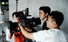 two men are filming another man in an orange shirt and white t - shirt with a camera