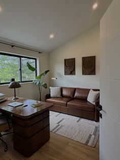 a living room filled with furniture next to a window and a wooden desk in front of a large window