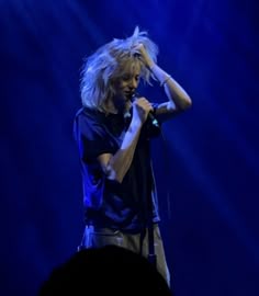 a man with long hair standing in front of a microphone and holding his hands up to his head