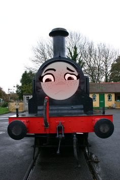 an old fashioned train with a face painted on it's front engine, sitting in a parking lot