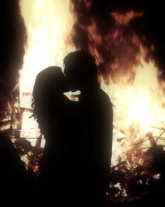 two people standing in front of a fire with their arms around each other as they embrace