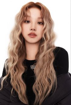 a woman with long blonde hair wearing a black jacket and posing in front of a white background