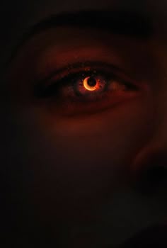 a woman's eye is glowing orange in the dark with red light coming from it