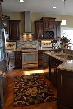 a kitchen with wooden floors and stainless steel appliances in the center, along with an area rug on the floor