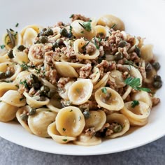 pasta with sausage and capers in a white bowl on a marble countertop, ready to be eaten