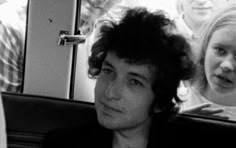 a black and white photo of a young man sitting in a car with two other people behind him