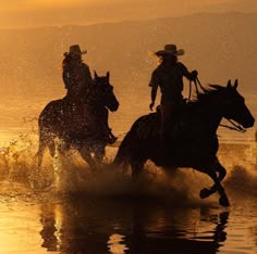 two people riding horses through the water at sunset