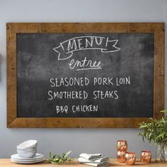 a chalkboard sign hanging on the wall above a dining room table with plates and utensils