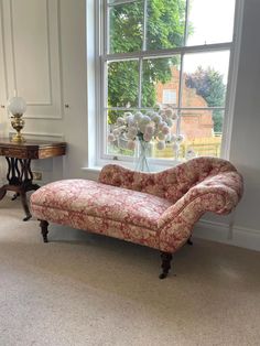 a couch sitting in front of a window next to a table with a vase on it