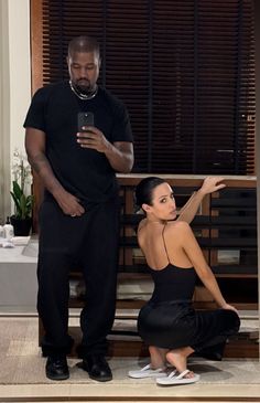 a woman kneeling down next to a man holding a cell phone in front of her