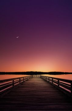 a wooden pier with the sun setting in the background and a half moon above it