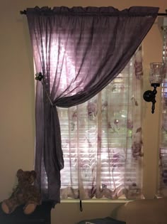 a teddy bear sitting in front of a window with purple drapes on it's windowsill