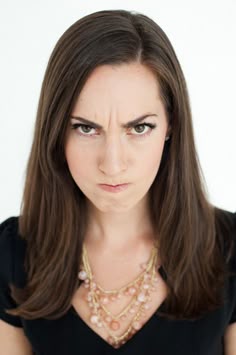 a woman wearing a necklace and black dress looking at the camera with an angry look on her face