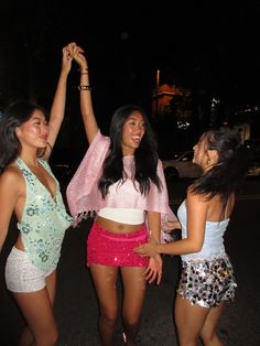 three young women are dancing in the street at night, one is holding her arm up
