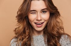 a woman with long, wavy hair smiles at the camera while wearing a gray sweater