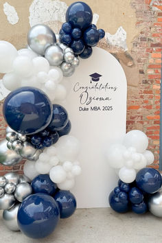 A white arch backdrop for a graduation party decorated with silver, white and navy blue balloons.