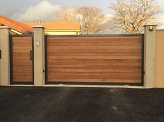 a large wooden gate in the middle of a driveway next to a house and trees