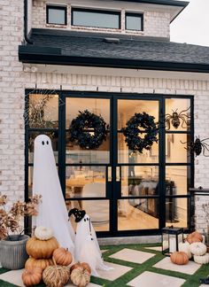 halloween decorations in front of a white brick house with black glass doors and pumpkins on the lawn