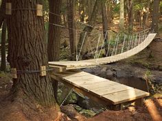 a wooden bridge in the middle of a forest next to a river and trees with ropes hanging from it