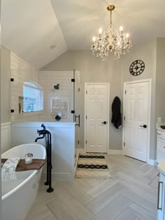 a bathroom with a tub, chandelier and white tile flooring in it