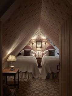 two beds sitting in a bedroom next to each other under a slanted ceiling with lights