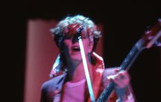a woman with curly hair holding a guitar in her hand and singing into a microphone