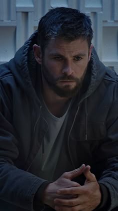 a man sitting on the ground looking at his cell phone while wearing a black jacket