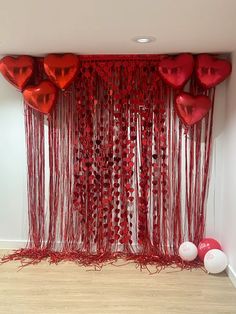 red balloons and streamers in the shape of hearts are hanging on a wall with white balls