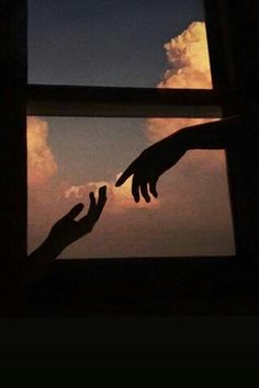 two hands reaching for each other in front of a window with the sky and clouds behind them