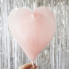 a heart shaped lollipop being held by a person's hand in front of a backdrop
