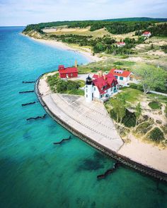 an aerial view of a red roofed house on the shore with clear blue water surrounding it