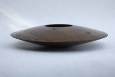 a wooden vase sitting on top of a white table next to a black object with holes in it