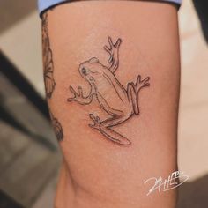 a small frog tattoo on the leg of a woman's thigh, showing it's front legs
