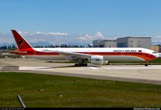 an airplane is sitting on the tarmac in front of some buildings and grass with mountains in the background