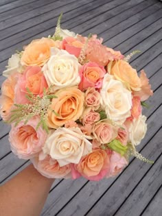 a bridal bouquet with peach, white and pink flowers on a wooden decking area
