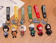 five keychains with anime characters on them sitting on a wooden table next to an open book