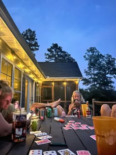 some people sitting at a table with cards and drinks on the outside deck, while one person holds up his leg
