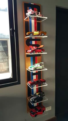 a wooden shelf filled with toy cars on top of a floor next to a window
