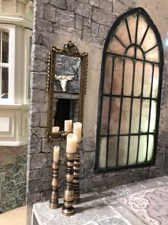 a table with candles on it next to a stone wall and a large stained glass window