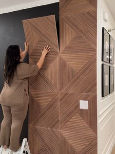 a woman standing on top of a step ladder next to a wooden paneled wall