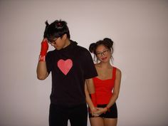 a man and woman standing next to each other in front of a white wall with a red heart on it