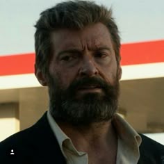 a man with a goatee and beard standing in front of a gas station sign