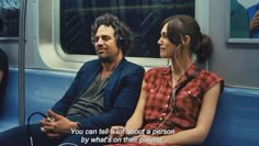 a man and woman sitting on a subway train looking at each other with ear buds in their ears