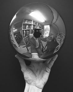 a person holding up a shiny ball in front of a black wall with bookshelves