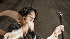 a woman with curly hair holding a baseball bat and wearing a black jacket while standing in front of a wall