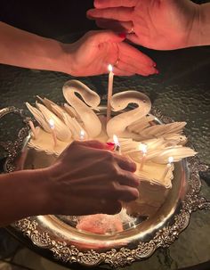 someone lighting candles on a swan shaped cake with two hands reaching for the one candle