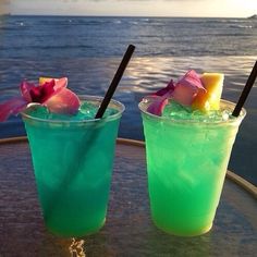 two drinks sitting on top of a table next to each other in front of the ocean