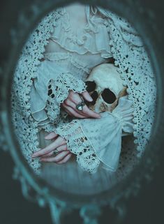 there is a woman holding a skull in her hand and wearing white laces on it