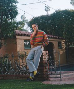 a man sitting on top of a brick wall in front of a fence and bushes
